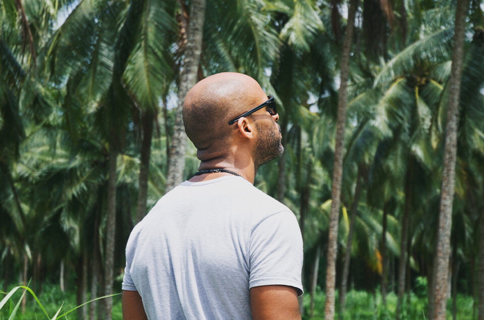 Matthew Hann standing on a coconut farm with coconut trees in the background, embodying sustainable business practices.