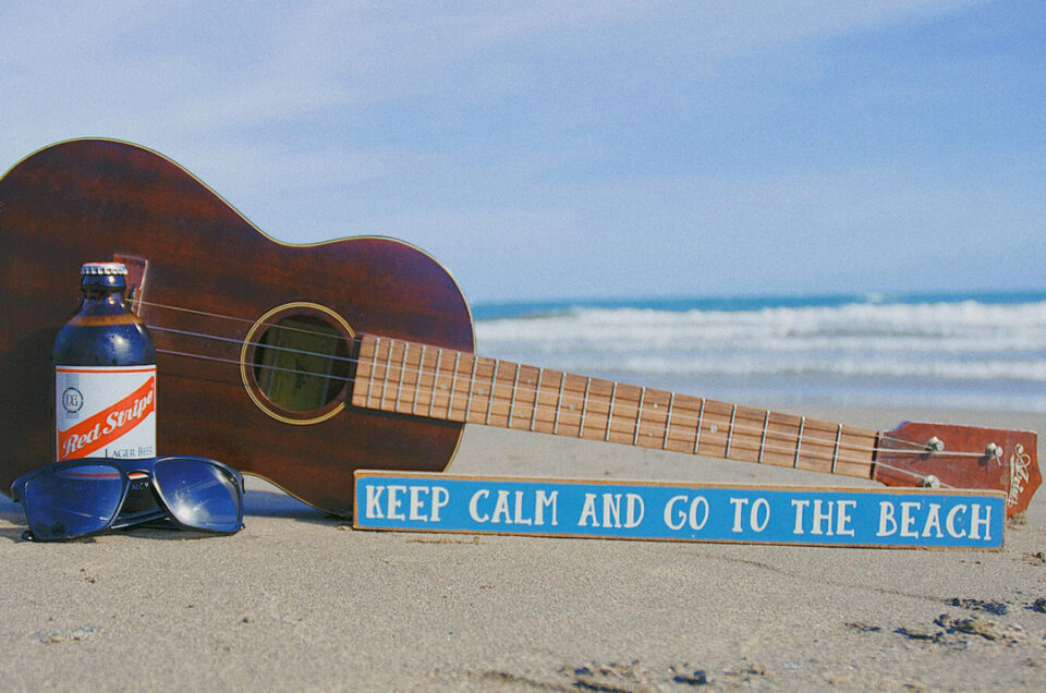 Red Stripe beer with a guitar and sunglasses on the beach, embodying the Jamaican vibe of relaxation and enjoyment.