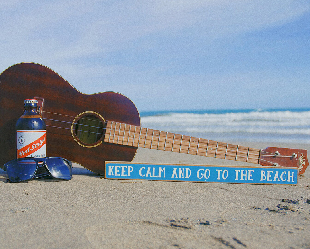 Red Stripe beer with a guitar and sunglasses on the beach, embodying the Jamaican vibe of relaxation and enjoyment.